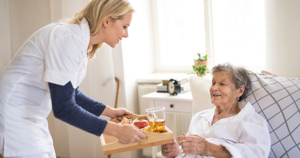 young health visitor bringing breakfast to a sick senior women